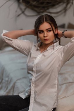 Beyaz, klasik kotlu, şık, güzel bir kadın. Yatak odasında oturuyor ve saçlarını düzleştiriyor. Odada siyah beyaz elbiseli çekici bir kız modeli var..