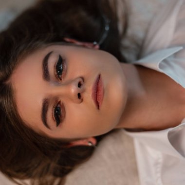 Güzel, gri gözleri, seksi dudakları, doğal makyajı ve şık beyaz bir klasik gömleği olan genç ve çekici bir kadının yakın plan yüzü. Odadaki yatakta tatlı bir kız yatıyor. Yukarıdan görüntüle.