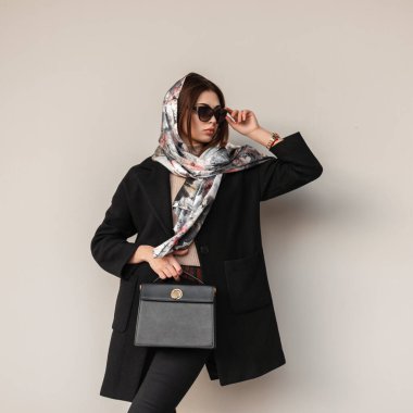 Şık, ipek şallı, siyah şık montlu, şık, şık ve şık bir genç bayan. Moda bir deri çantalı. Kapalı bir yerde duvarın yanında klasik güneş gözlüklerini düzeltiyor. Şık, modern, profesyonel kız model..