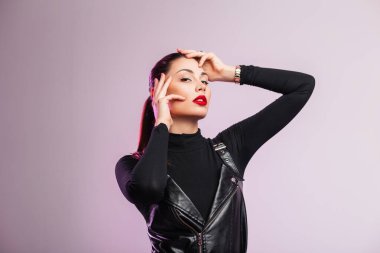 Stüdyo moda portresi şık, seksi kırmızı dudaklı, kahverengi saçlı, siyah, modaya uygun deri elbiseli, açık renk arka planda güzel bir genç kadın. Modern kız tarzı model içeride poz veriyor..