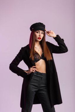 Modern kız mankeni, moda siyah şapkayı içeride düzeltir. Şık dantel iç çamaşırlı, şık ceketli, şık, şık, genç bir kadın. Stüdyoda seksi kırmızı dudaklı, duvarın yanında..