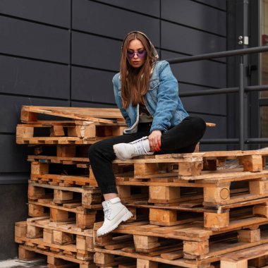 Havalı, havalı, havalı, kotlu, menekşe renkli gözlüklü, beyaz çizmeli, şık bir hippi kadın. Sokakta duvarın yakınındaki ahşap paletlerde oturuyor. Güzel bir kız.