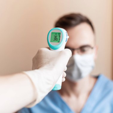 Sıcaklık doktorunu tıbbi bir maskeyle ölçüyor. Virüs Covid-19 'u kontrol et. Güvenlik kontrolü için dijital termometre kullanın..