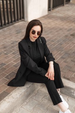 Genç, zarif kadın ceketleri koleksiyonu. Modaya uygun siyah ceketli, iş pantolonlu ve tişörtlü şık bir kadın sokakta oturuyor..