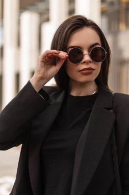 Yakın plan kadın yüzü, temiz ten, seksi dudaklar, doğal ruj rengi güneş gözlüğü. Siyah şık elbiseli çekici kız mankeni bahar günü caddelerde bardakları düzeltiyor..