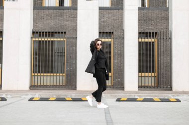 Resmi takım elbiseli, beyaz ayakkabılı, şık siyah elbiseli güzel bir kadın modern bir binanın yanında yürüyor.