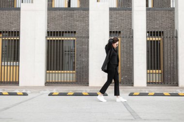 Şık güneş gözlüklü şık bir genç bayan şık bir gençlik ceketi giyiyor ve şehrin klasik binasının yakınında geziyor. Gündelik kıyafetlerle gezen güzel, modern model kız..
