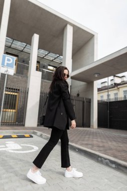 Eski moda güneş gözlüklü, modern binanın yakınında duran deri çantalı, şık, şık, genç bir kadın. Sokakta siyah ceketli çekici trend kız hipster..