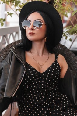 Kafede deri ceketli, güneş gözlüklü şapkalı, siyah yaz elbisesi içinde oldukça şık bir kadın portresi. Siyah elbiseli güzel kız yaz terasında eski bir sandalyede dinleniyor..