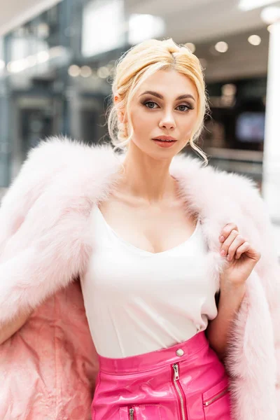 奢华的欧洲金发女青年穿着时髦的粉色皮衣 上装典雅的白色上衣 穿着时髦的皮裙 摆设在商场中央 现代可爱的时髦女模特走在商店里 冬季时尚 — 图库照片