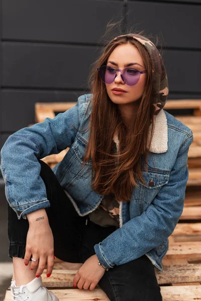 Mujer hipster con estilo joven fresco en ropa juvenil casual de moda en  gafas moradas de moda posa en la ciudad. modelo de moda de chica glamorosa  sexy estadounidense se sienta en