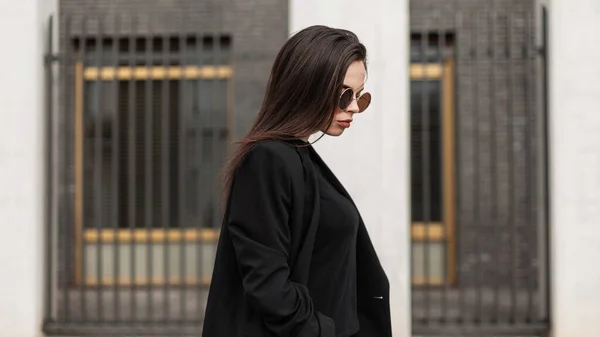 一个戴着墨镜 身穿黑色正装和夹克的漂亮优雅姑娘在城市里行走的画像 — 图库照片