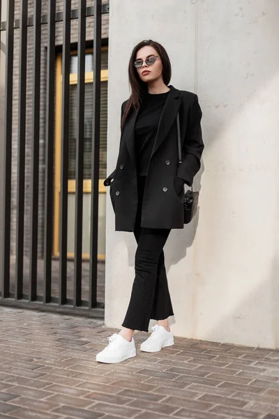 女用青年休闲装 穿着黑色T恤衫的时髦年轻漂亮的女人 穿着漂亮典雅的黑色时髦夹克 在街上的墙上挂着时尚手提包 黑色风格 — 图库照片