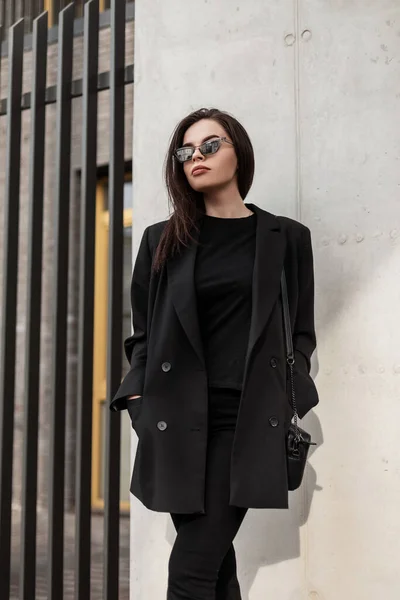 女性のためのファッショナブルな服 通りの壁の近くにハンドバッグと美しいエレガントな黒のスタイリッシュなブレザーで黒のヴィンテージTシャツのファッション若い女性 ブラック スタイル — ストック写真