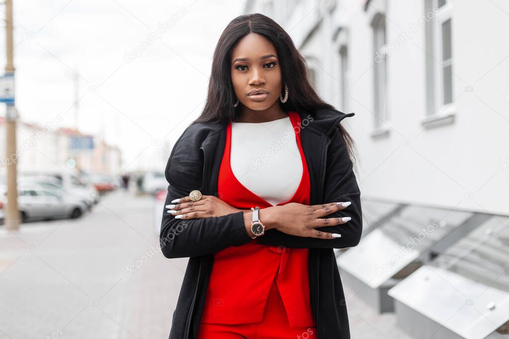 Street portrait beautiful young African woman with long hair with clean skin with sexy lips in stylish elegant clothes outdoors near vintage building. Attractive black girl in trendy outfit in city.
