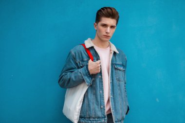 Moda mankeni, şık pembe kazaklı, şık mavi kot ceketli, kentin renkli duvarının yanında klasik kumaş alışverişçisi olan yakışıklı bir adam. Modayı takip eden iyi bir adam açık havada giyiniyor. Gençlik tarzı.