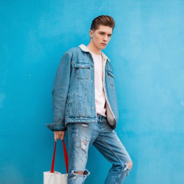 Tarz sahibi, genç, şık kotları olan, çekici, güzel pembe kazağı olan yakışıklı genç bir adam arka plandaki mavi duvarda duruyor. Moda mankeni şehirde oldukça seksi görünüyor..