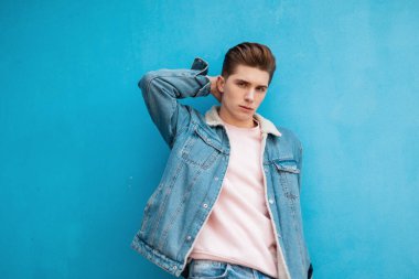 Şık genç adam saç stili, şık kotlar, göz kamaştırıcı güzel pembe tişörtler, arka planda mavi duvarlar. Sokak kıyafetleri içinde modaya uygun erkek modeli.