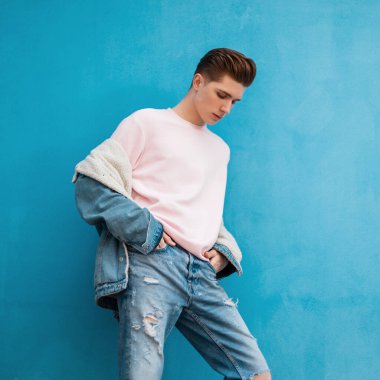 Şehrin mavi arka planında poz veren yeni gençlik koleksiyonundan şık kotlar giyen modern genç adam. Çekici, çekici bir adam caddedeki klasik duvarın yanında dikiliyor. Yaz stili.