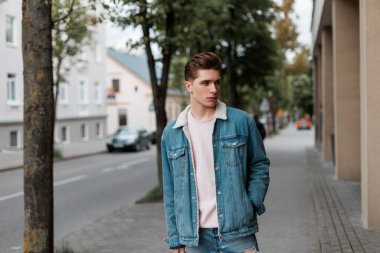 Pembe tişörtlü, modaya uygun mavi pantolonlu, şık, genç bir adam yol kenarında yürüyor. Şık giyinmiş yakışıklı adam şehirde seyahat ediyor. Modaya uygun yaz erkek giyimi..