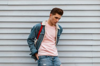 Moda mankeni, şık pembe kazaklı, şık mavi kot ceketli, kentin klasik beyaz duvarının yanında kumaş alışverişi yapan yakışıklı bir genç. Açık havada şık giyinen şehirli bir adam. Gençlik tarzı.