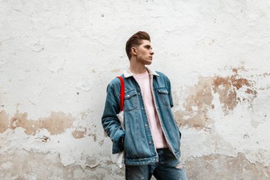 Moda mankeni, şık pembe tişörtlü, modaya uygun mavi kot ceketli, kentin klasik duvarının yanında kumaş alışverişi yapan yakışıklı bir genç. Açık havada şık giyinen şehirli bir adam. Gençlik sokak stili.