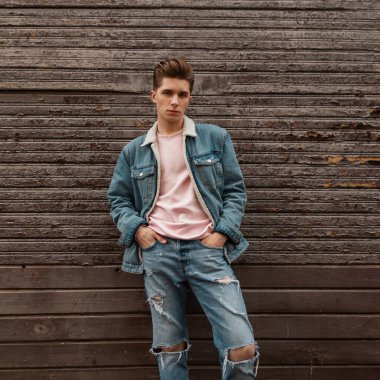 Pembe şık tişörtlü, kot pantolonu mavi ceketli yakışıklı genç adam caddedeki ahşap vintage binanın yanında duruyor. Yakışıklı, modacı, şehirde saç stili olan bir model..