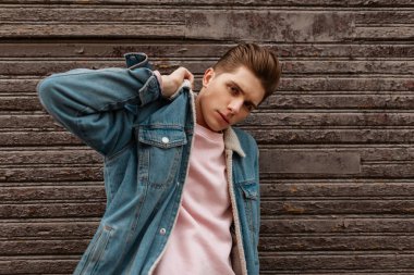 Çok yakışıklı genç bir adam şık gençlik kıyafetleriyle şık bir şekilde giyiniyor. Göz kamaştırıcı güzel pembe tişörtler giyiyor. Sokakta eski moda tahta duvarın yanında poz veriyor. Avrupalı moda adamı şehirde manken.