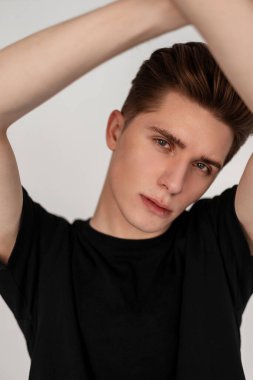 Moda tarzı saç stili, güzel gri gözlü, temiz sağlıklı tenli, modaya uygun siyah tişörtlü beyaz arka planda genç çekici bir adam portresi. Odada poz veren yakışıklı bir adam..