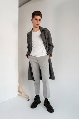 Beyaz tişörtlü, modaya uygun, ekoseli, şık pantolonlu, şık, siyah çizmeli genç, modaya uygun bir adam stüdyoda duvarın yanında duruyor. Moda gündelik kıyafetleriyle yakışıklı, modern bir erkek mankeni odada.
