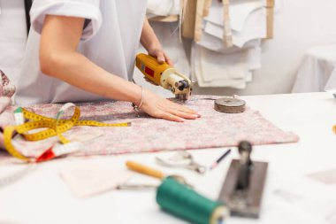 Elektrikli terzi stüdyodaki kumaşı kesiyor. Çalışma sürecinde bir moda tasarımcısının çalışma yeri