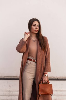 Zarif kahverengi elbiseli, deri çantalı, caddede klasik beyaz bir binanın yanında poz veren oldukça çekici genç bir model. Açık havada günlük kıyafetli güzel bir kız. Bayan..