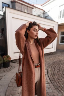 Moda mankeni, modaya uygun mevsimlik giysiler içinde seksi genç bir kadın bahar günü şehirde dikilen saçları düzleştiriyor. Deri çantalı, şık kıyafetli, dışarıda poz veren güzel bir kız. Şehir kadını..