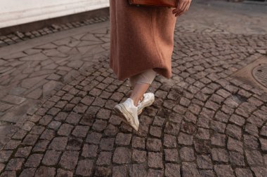 Şık deri spor ayakkabılı kadın bacakları eski taş yolda yürüyor. Şık, uzun paltolu şık ayakkabılı şık bir kız sokakta yürüyor. Bahar kadınlarının moda gündelik ayakkabıları
