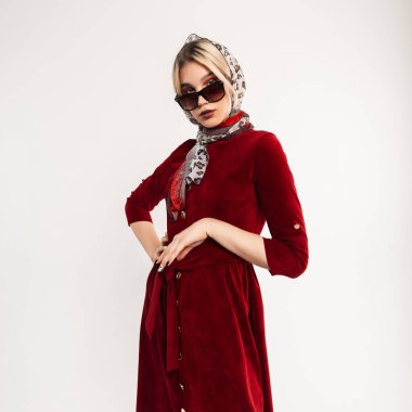 Şık güneş gözlüklü, kafasında leopar desenli atölye eşarplı, bordo elbisesiyle stüdyodaki beyaz vintage duvarın yanında poz veren lüks bir genç kadın. İçerideki çekici sarışın kız. Seksi bayan..
