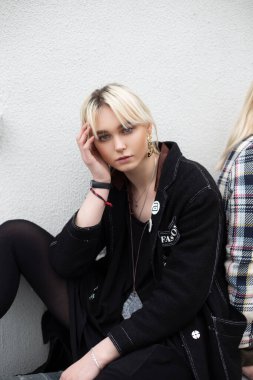 Moda mankeni siyah giysili güzel sarışın kadın klasik binanın yanındaki sokakta dinleniyor. Siyah kıyafetli modern genç kız şehirde oturuyor. Genç kadın kıyafetleri..