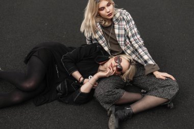 Şehirdeki basketbol sahasında dinlenen şık giyimli iki kız kardeş. Güneş gözlüklü, siyah, modaya uygun bir model damalı ceketli seksi kız kardeşin üzerinde yatıyor..