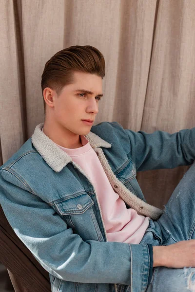 流行の若い男が流行のジーンズでヴィンテージデニムジャケットで髪型が通りに残ります ファッショナブルなユースブルーデニムの服でスタイリッシュな本格的な男モデル屋外 新しいコレクションからカジュアルメンズウェア — ストック写真