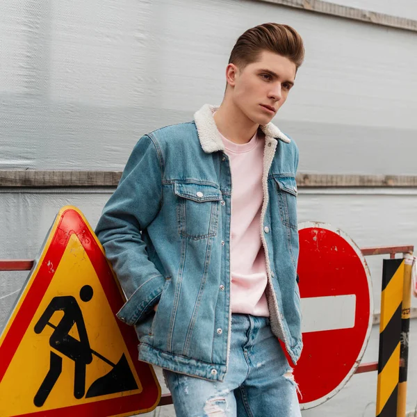 Glamorous trendy young man in ripped jeans in blue denim jacket