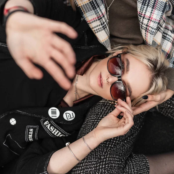 时尚模特穿着老式黑色衣服 戴着太阳镜的年轻姑娘躺在床上 用手捂住相机 酷时髦的女朋友们在人行道上休息 青少年街头风格 — 图库照片