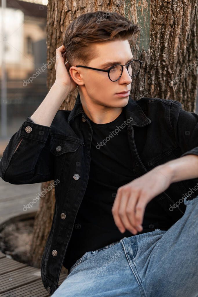 Hombre joven bastante urbano con estilo en ropa de jeans de moda en zapatillas  negras de moda con mochila de cuero