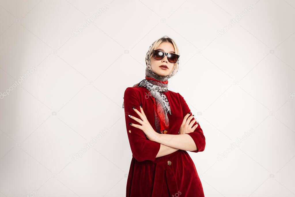Sexy business fashionable young woman in fashion sunglasses in burgundy elegant dress with vintage leopard scarf on head posing indoors. Stylish studio portrait blonde girl in trendy outfit in room.
