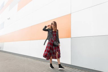 Şık güneş gözlükleriyle gülümseyen, şık siyah elbiseli, sıradan ayakkabılı modern duvarın yanında sokakta çanta taşıyan güzel, şık genç bir kadın modeli. Neşeli gülümseyen kız yürümekten hoşlanıyor..