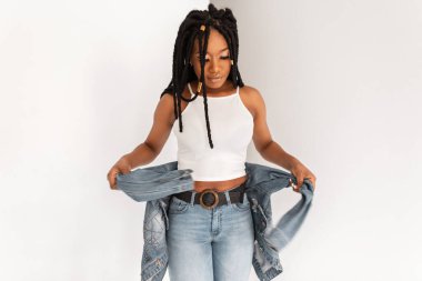 Moda giysileri içinde modern saç stili rastalı çekici siyah kadın stüdyoda beyaz arka planda klasik mavi kot ceket giyiyor. Odada poz veren güzel Afrikalı Amerikalı kız..