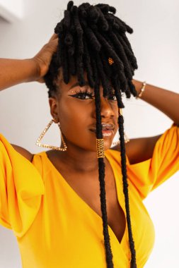 Güzel, çekici, genç, siyah, moda, sarı güzellik elbisesi içinde bir model. Stüdyodaki beyaz arka planda modern, şık, rastalı saç stilini düzeltiyor. Yakın plan afro kız portresi.