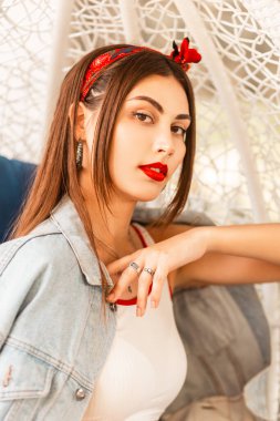 Kırmızı rujlu, seksi dudaklı, şık bandanalı, genç mavi kot ceketli, çekici bir kızın portresi. Terasta bir kafede eski bir koltukta yeni bir koleksiyon..