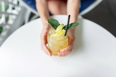 Terasta beyaz bir masada eski bir kupada limonata. Dişi eller sarıyı tutar taze soğuk limonata içerler naneli