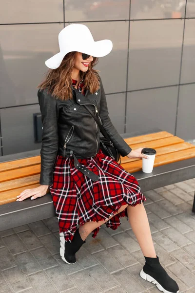 幸せな都会のヒップスター女の子で流行の服でベンチに座ってコーヒーを飲む — ストック写真