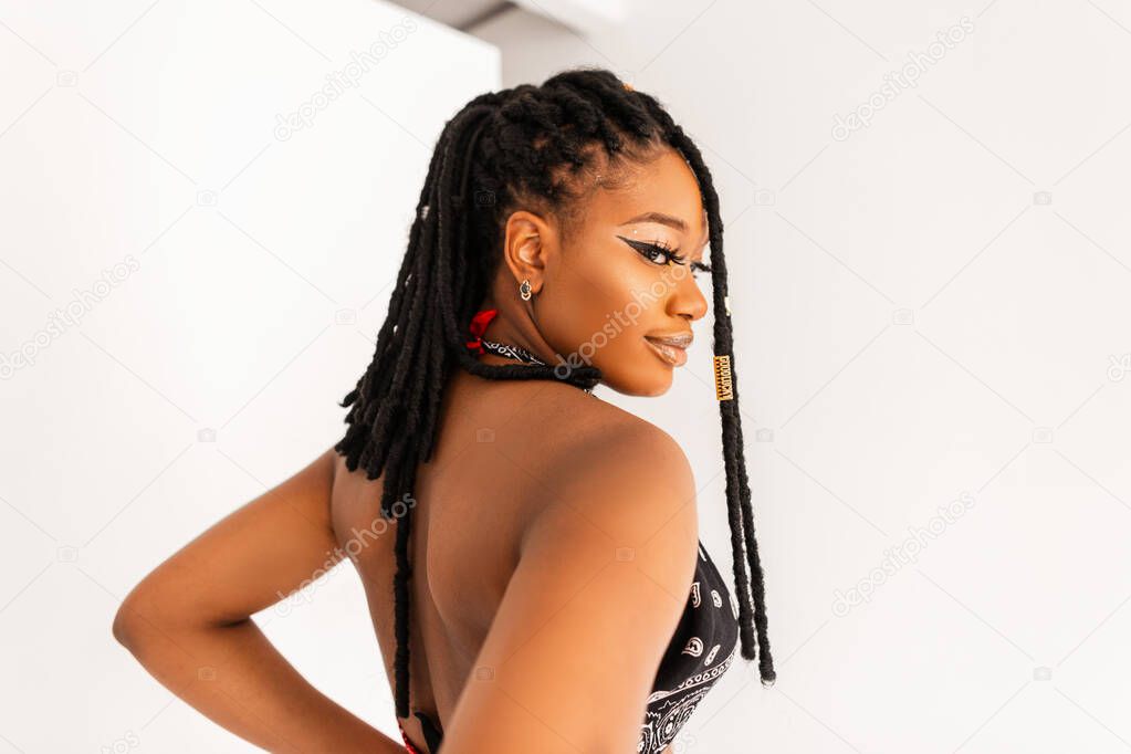 Portrait of sexy beautiful young black woman with cool dreadlocks in stylish bandana top with open back on white background indoors. Attractive African girl fashion model in studio.