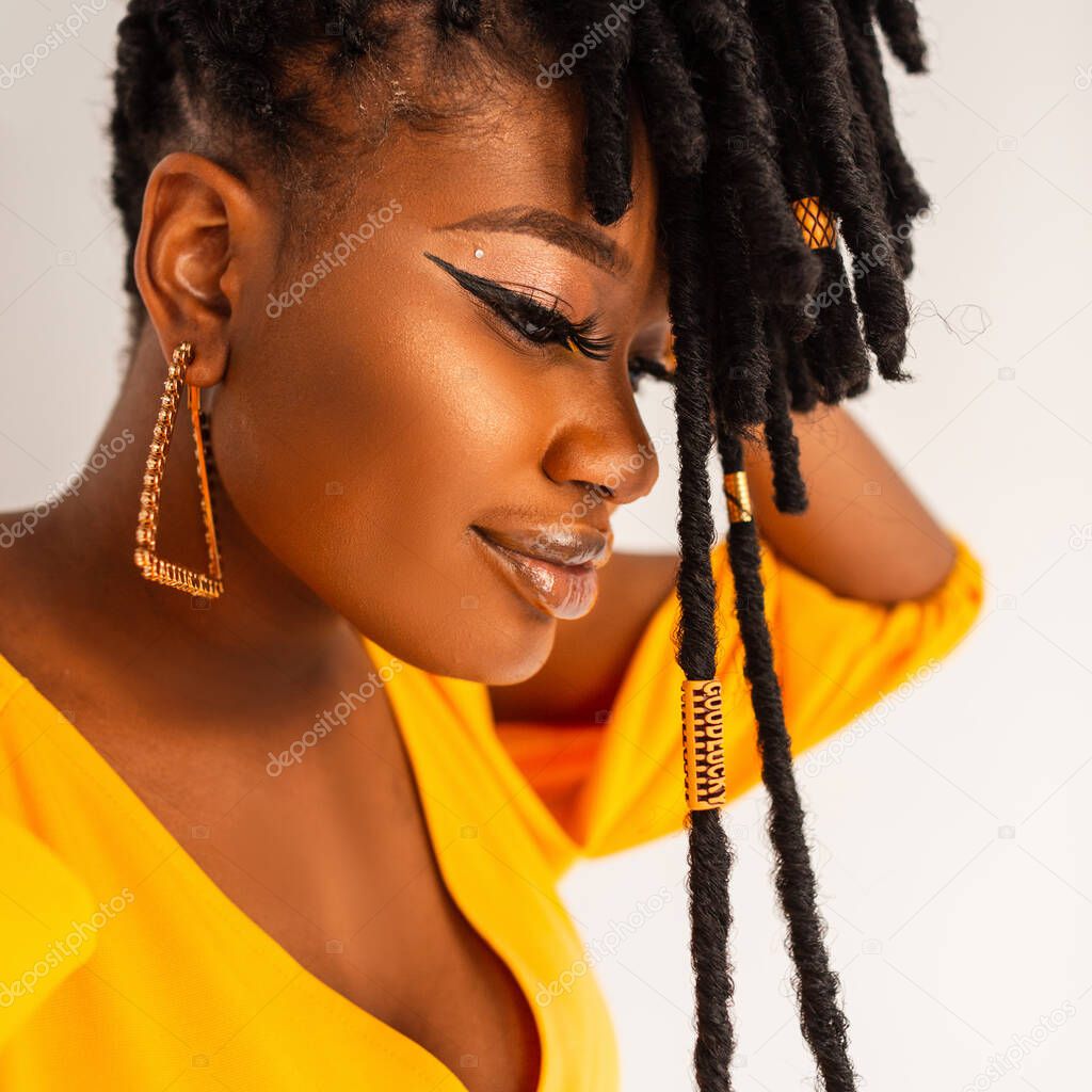 Fashion portrait of beautiful happy african girl with long dreadlocks hairstyle in fashionable yellow dress with gold earrings